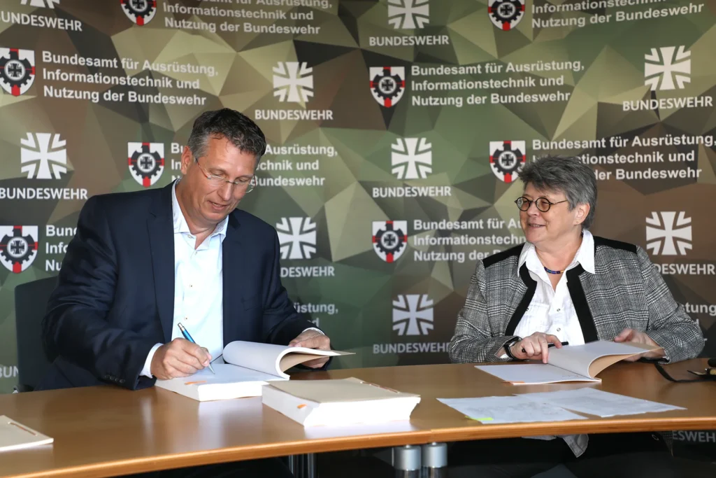Die Vizepräsidentin des BAAINBw Annette Lehnigk-Emden unterschreibt gemeinsam mit dem Geschäftsführer der Firma M. Schall GmbH & Co. KG, Markus Schall, die Verträge.