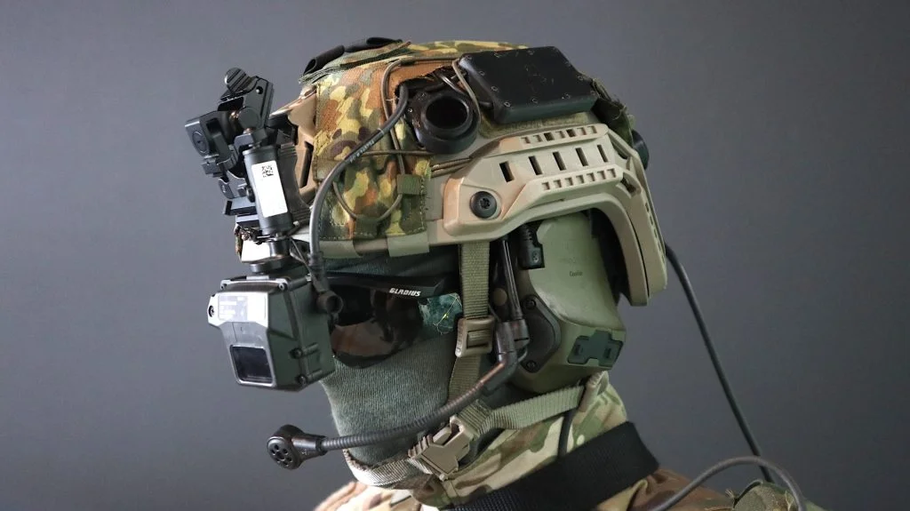 Der "Infanterist der Zukunft" trägt eine Menge digitaler Unterstützung: Um den Gefechtshelm mit Tarnbezug finden sich ein aktiver Gehörschutz samt Mikrofon, Laser-Warngerät und ein Head-up-Display THEA von THEON.