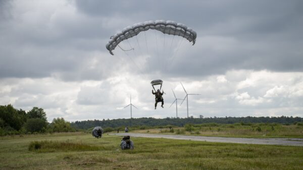 Das Team vom Tandemsprung befindet sich im Landeanflug, die Knie sind leicht gehoben. Im Hintergrund packen bereits Freifallspringer ihre Fallschirme zusammen.