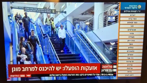 Wird ein Angriff auf Israel gestartet, reagiert das nationale Raketenwarnsystem. So warnt beispielsweise das Fernsehen, welche Städte und Regionen (Liste rechts im Bild) gefährdet sind. Die Bewohner dort werden zudem aufgefordert, Schutz zu suchen (Zeile am unteren Bildschirmrand).