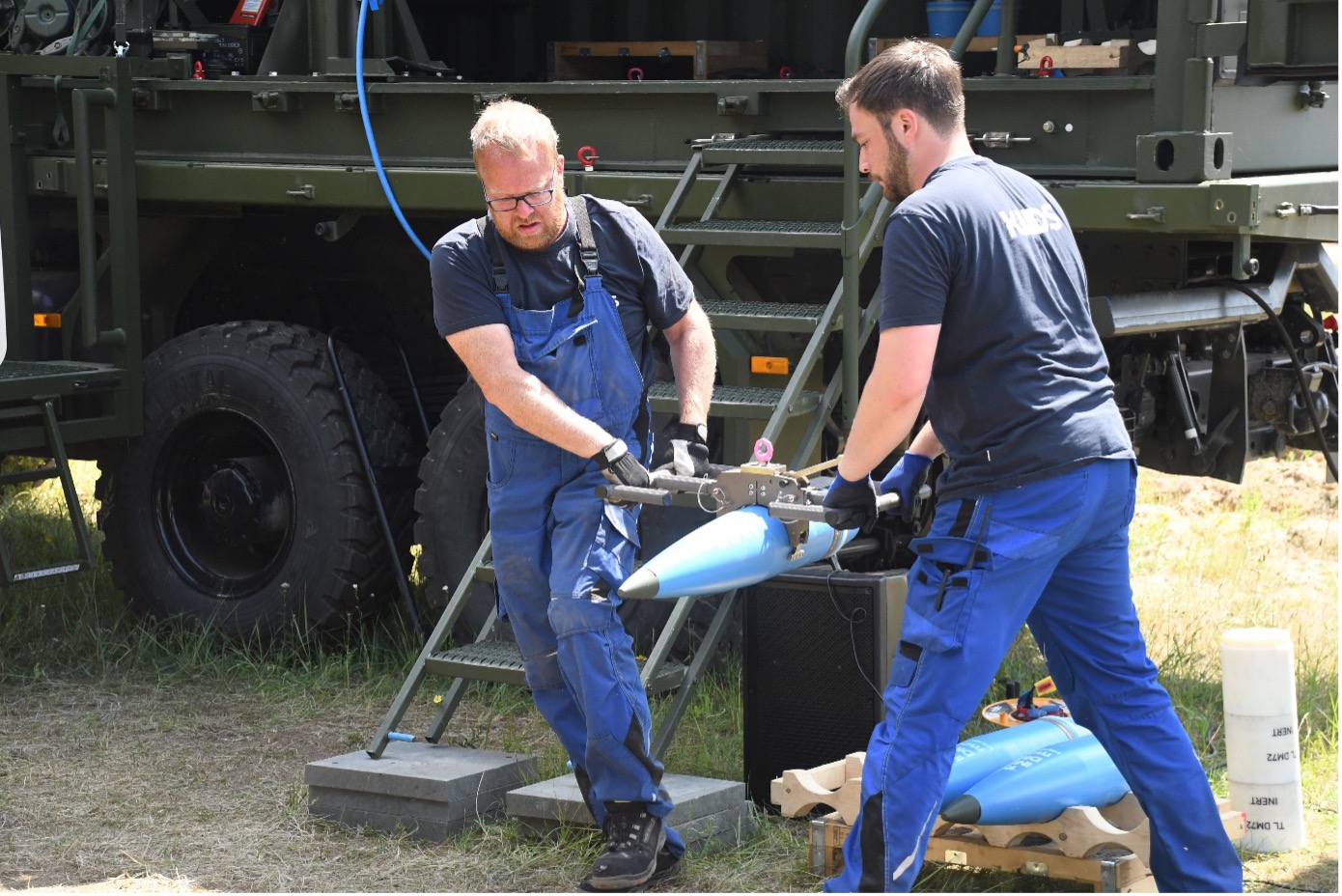 Modernes Aufmunitionierungskonzept für Artilleriegeschütze: Zwei Mitarbeiter heben eine Granate mit der Beladezange. Dieses soll die Personen schützen und den Transport einfacher und sicherer gestalten.